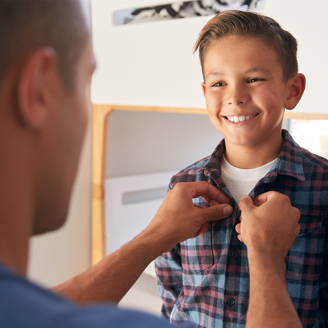 father helping young son button his shirt