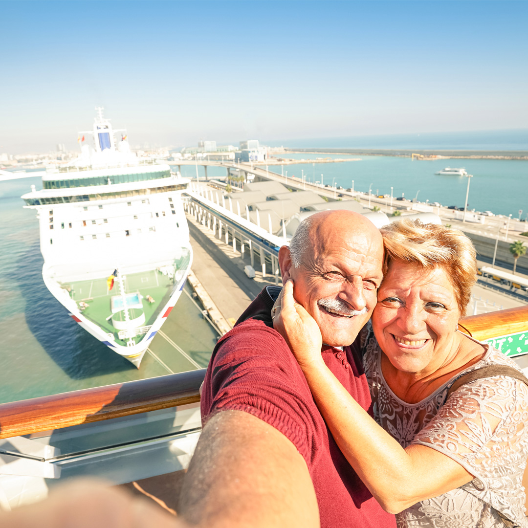 Man and woman taking selfie with a cruise ship in the background